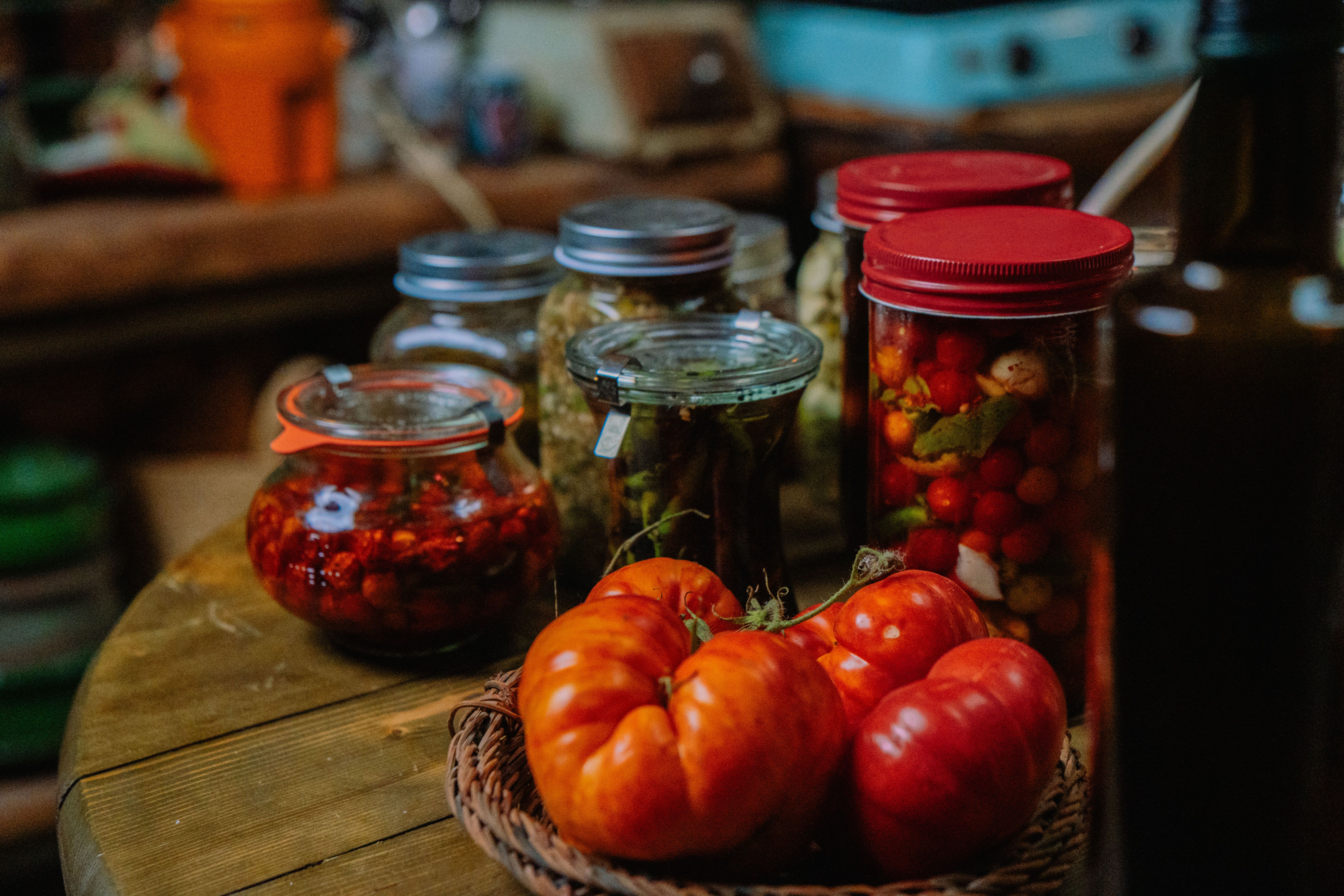 A rustic kitchen setup featuring fresh tomatoes and various pickled vegetables in glass jars.